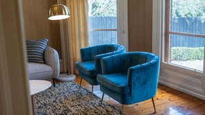 Quarto com poltrona azul, mesa redonda, luminária de chão e vista para o exterior.