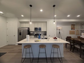 A modern kitchen with a central island, bar stools, and a dining area with chairs. - Modern 3B/2.5BA Townhouse in East Colorado Springs (Colorado Springs)