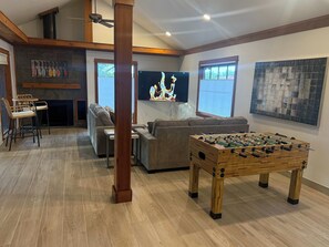 A spacious living room with a wooden floor, a sofa, a coffee table, a television, and a foosball table. - Lakehouse Escape - Hot Tub - Fire Pit  - Eureka Springs (Eureka Springs)