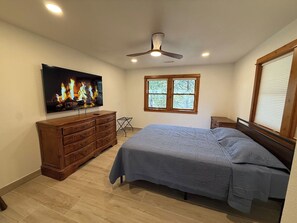 A bedroom with a bed, dresser, television, and a window with blinds.
