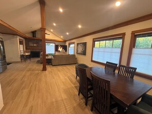 A spacious living area with a wooden dining table and chairs, a fireplace, and large windows. - Lakehouse Escape - Hot Tub - Fire Pit  - Eureka Springs (Eureka Springs)
