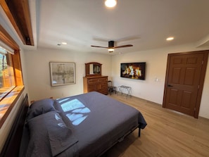 A bedroom with a bed, a ceiling fan, a dresser, a chair, and a door.