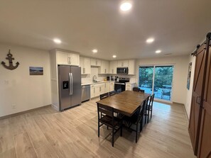 A modern kitchen with white cabinets, a stainless steel refrigerator, and a wooden dining table.