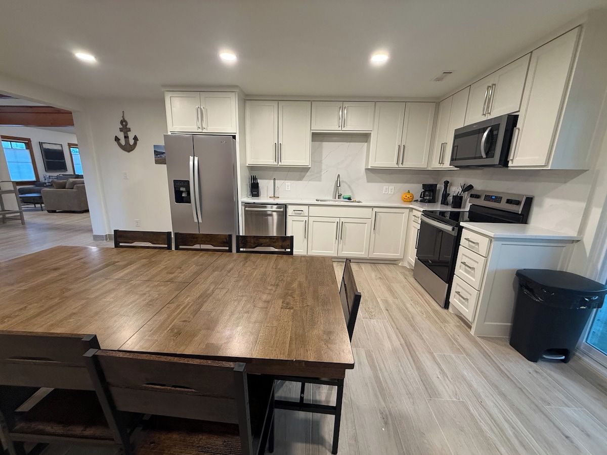 A modern kitchen with white cabinets, stainless steel appliances, and a wooden dining table.