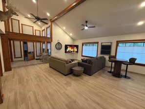 A spacious living area with a fireplace, ceiling fans, and a large window. - Eureka Springs Lake Lodge sleeps 14 - Hot Tub (Eureka Springs)