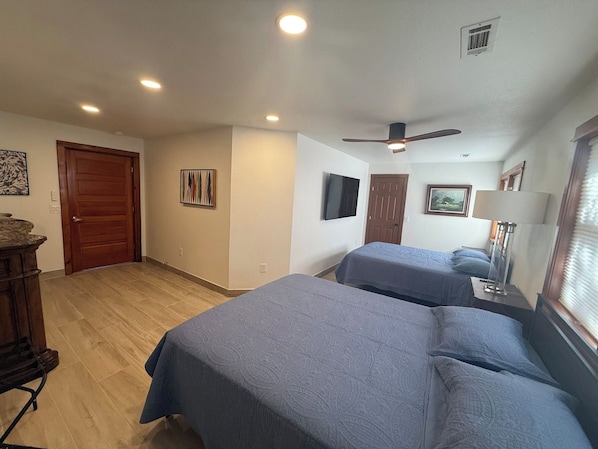 Habitación de hotel con dos camas, ventilador de techo, televisor y cómoda de madera.