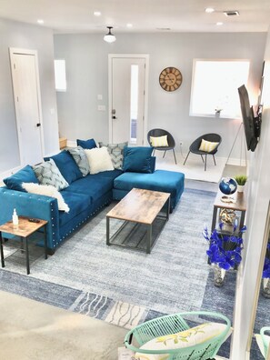 Una sala de estar moderna con un sofá seccional, una mesa de centro, una mesita auxiliar pequeña, un globo decorativo y un tapete azul estampado.
