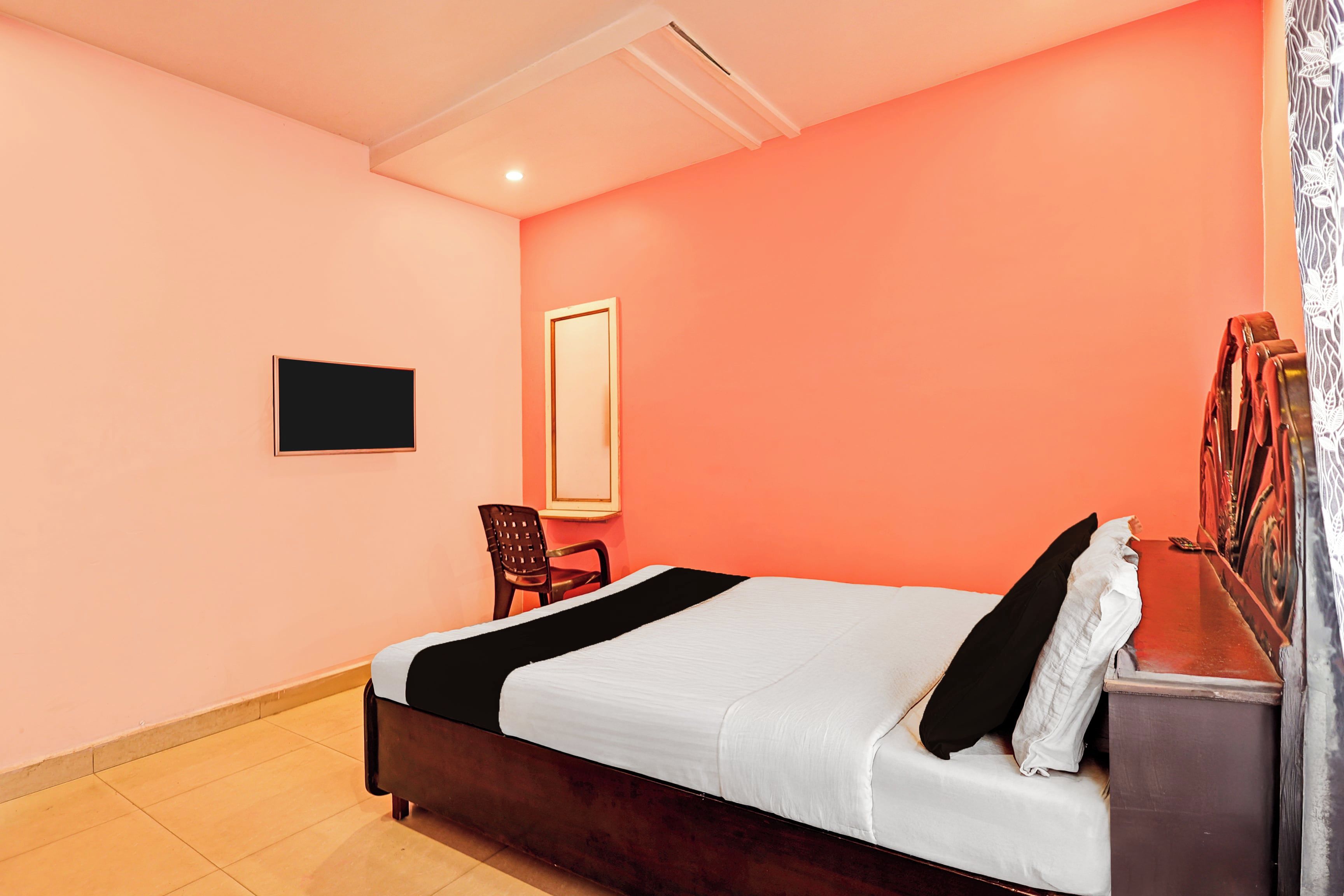Un dormitorio con una cama, una silla, un televisor y una ventana con cortinas.