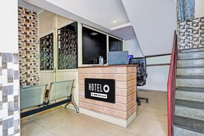 A hotel reception desk with a sign indicating it is serviced by OYO. There is a laptop on the desk, a chair, and a bench with a metal mesh backrest. - Hotel O Vizag Centre Formerly Sri SaiInn (Visakhapatnam)
