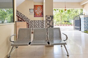 Un área de espera con tres sillas de metal, una escalera con baldosas estampadas y un calendario en la pared.