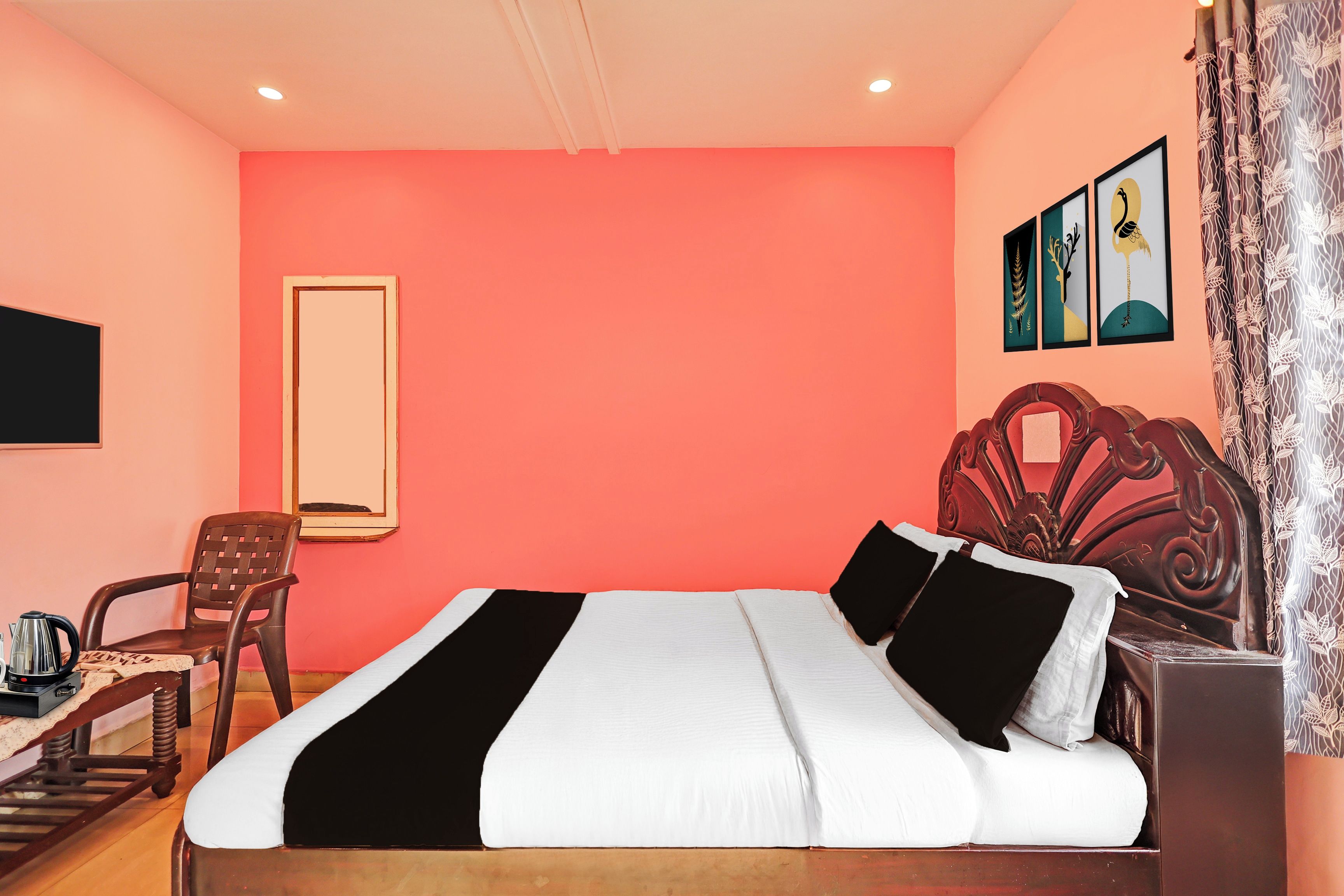 A hotel room with a single bed, a wooden headboard, a chair, a table with a kettle, and a wall-mounted TV.