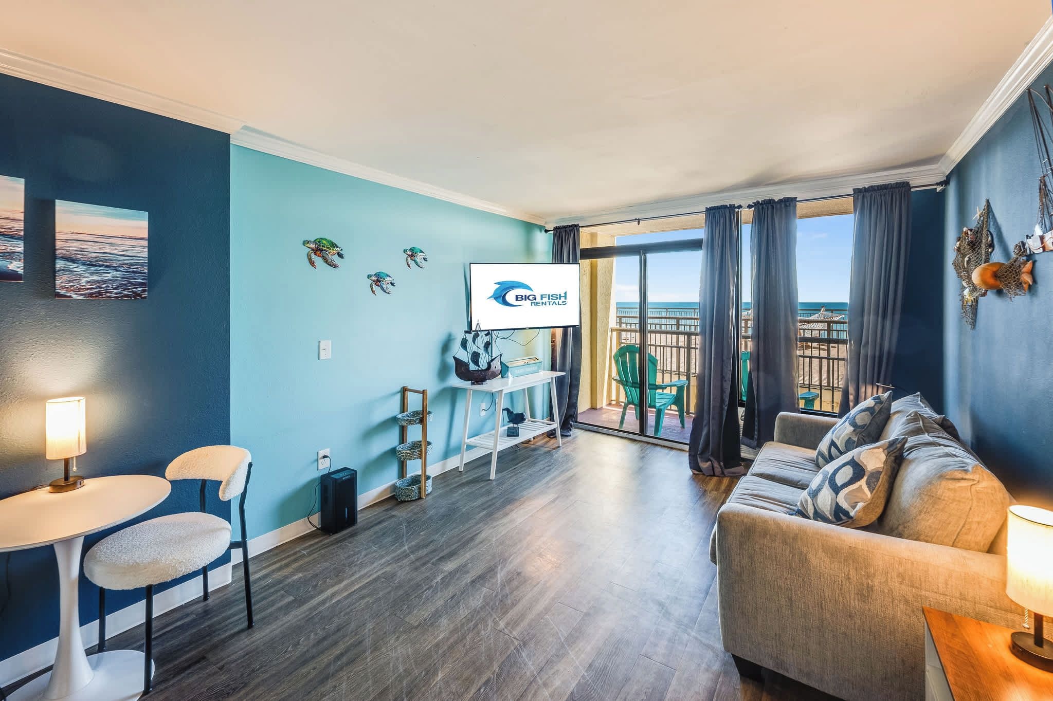 A modern living room with a sofa, chairs, a TV, and a view of the beach.