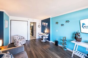 Un salon moderne avec un canapé, un coin repas avec des chaises, une cuisine en arrière-plan et un mur orné d’un logo.