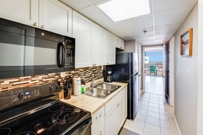 Cocina moderna con microondas, estufa y refrigerador. Cuenta con un salpicadero de azulejos y vistas al balcón.
