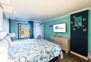 Un dormitorio con cama, cómoda, televisor y vista al exterior.