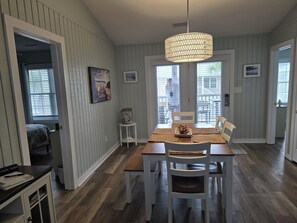 Un espace repas avec une table en bois, des chaises blanches et un luminaire suspendu.