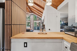 A modern kitchen with a wooden island, pendant lights, and a view to the outdoors. - La Cabaña. A Redwood Retreat with Hot Tub & Starry Nights (Pioneer)