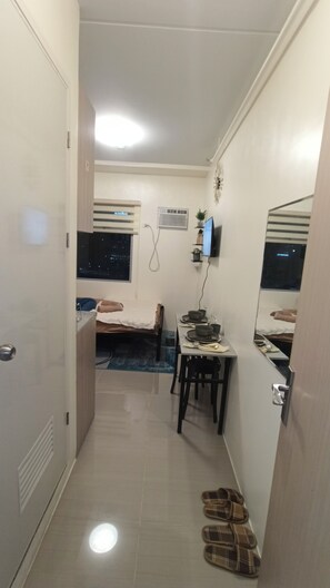 A compact room with a bed, a desk with a computer, a chair, and a pair of slippers on the floor. - Cozy 1-bedroom Apartment in Delightful Quezon City with AC (Quezon City)