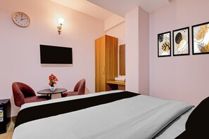 A hotel room with a bed, a desk with a chair, a wall-mounted TV, a clock, and framed artwork. - Collection O BapatSquareFormerly Riboila (Indore)