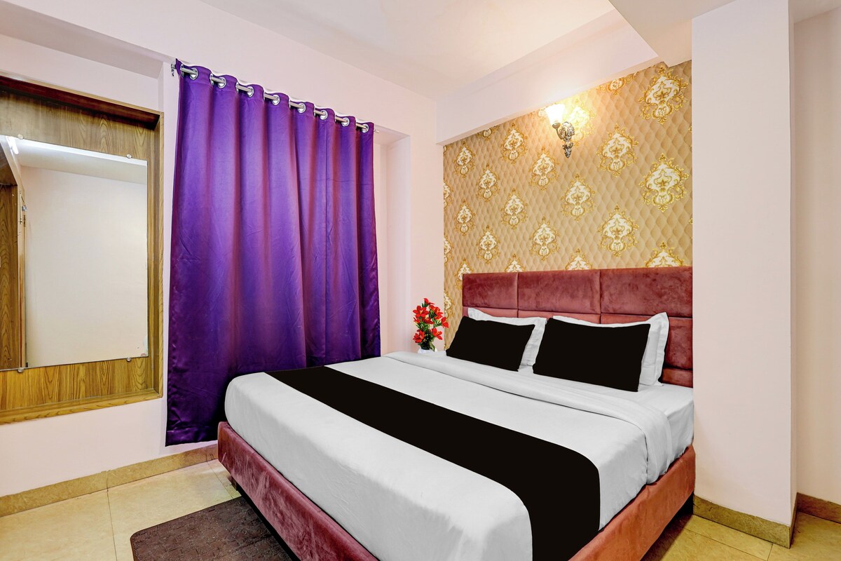 A hotel room with a bed, purple curtains, a patterned wall, and a window with a view.