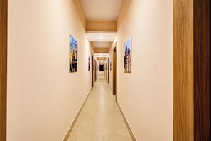 A long, narrow hotel corridor with a tiled floor and walls adorned with framed pictures. - Collection O BapatSquareFormerly Riboila (Indore)