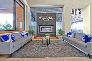 A modern lobby with two sofas, a patterned rug, a small table with a plant, and a wall with a sign reading 'Regal Oaks by IDILIQ'. - Regal Oaks Resort | Near Disney & Old Town (Kissimmee)