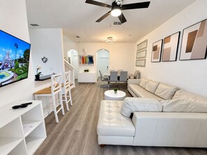 Un salón moderno con un sofá blanco, una mesa de centro y un televisor montado en la pared.