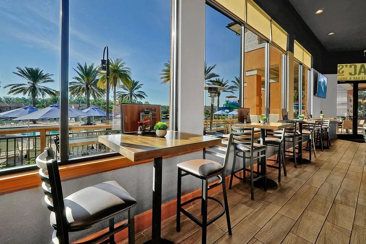 A restaurant with outdoor seating, large windows, and a view of palm trees.