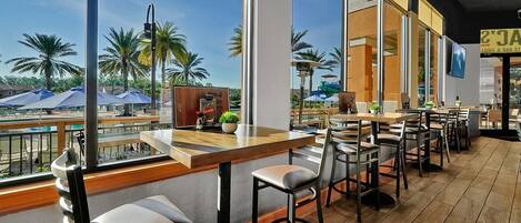 A restaurant with outdoor seating, large windows, and a view of palm trees.