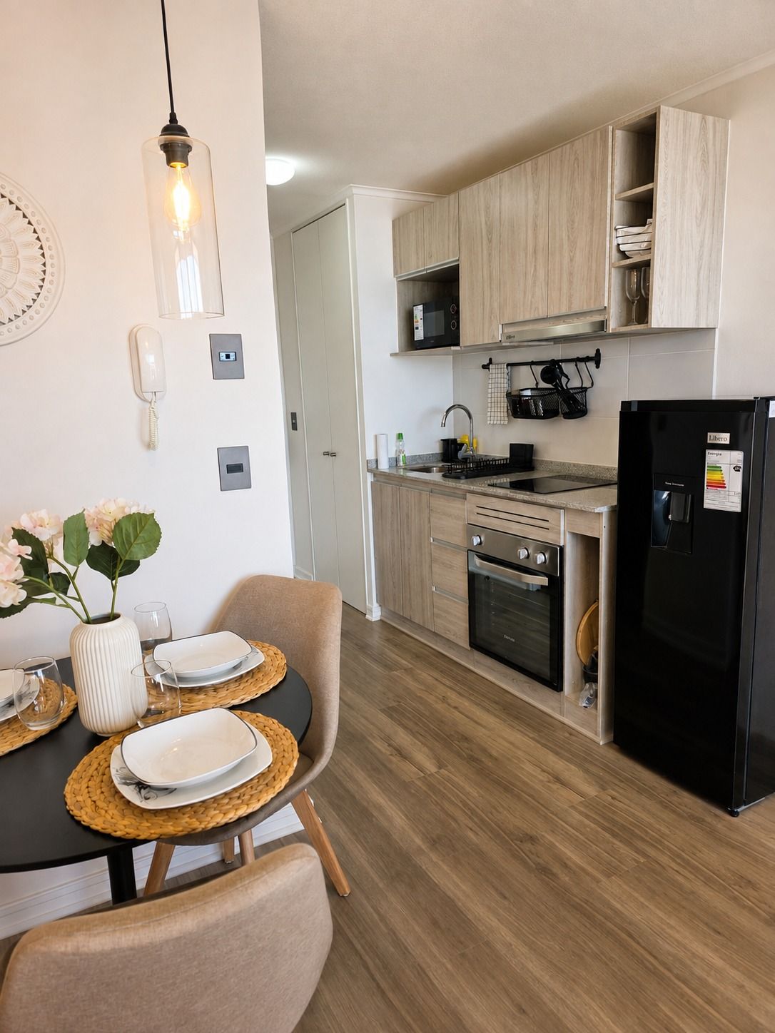 A modern kitchen with wooden cabinets, a black refrigerator, and a dining area with a table set for two.