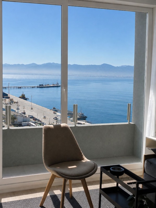 Una habitación con un ventanal grande que da a la costa, una silla y una mesita.