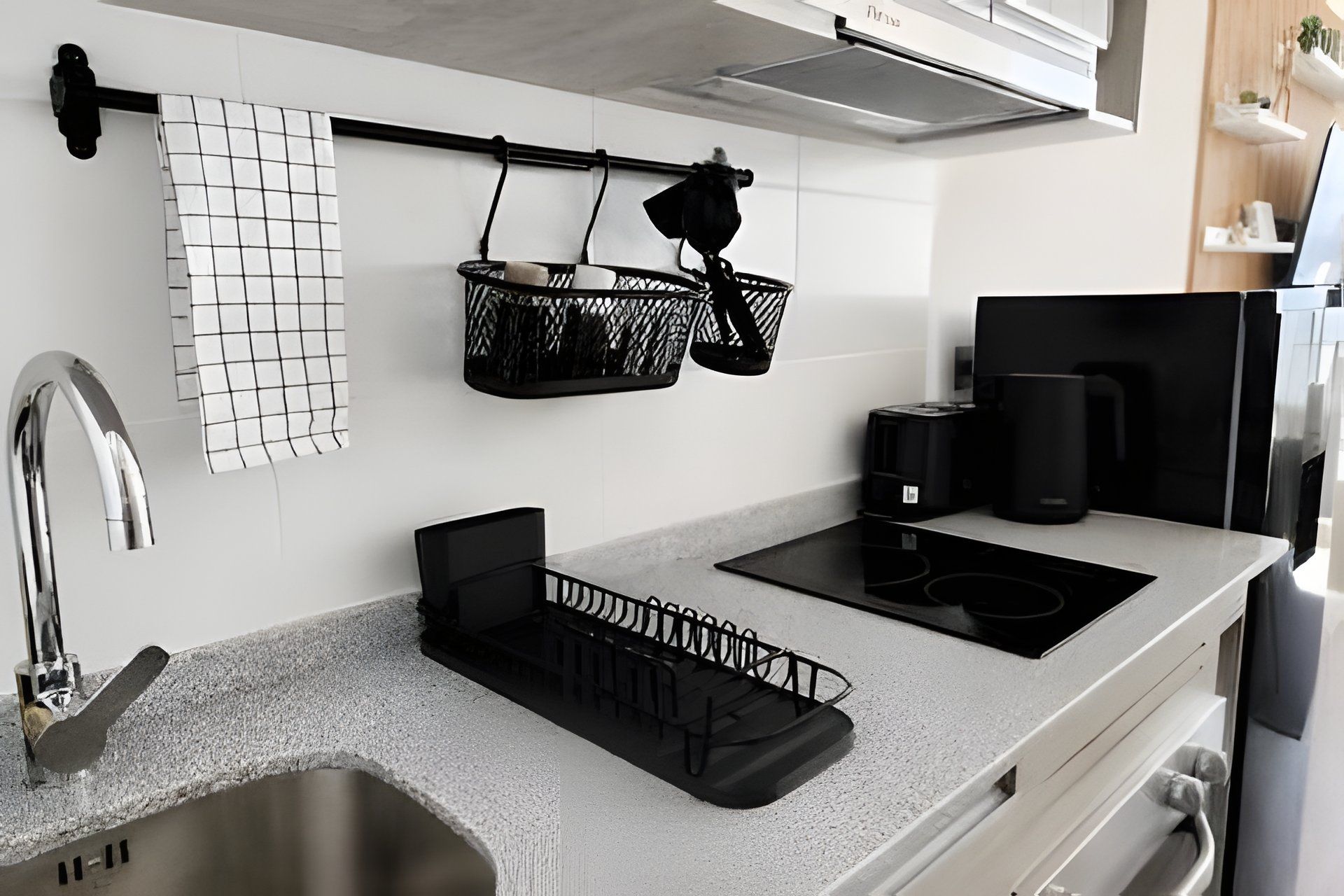 A modern kitchen with a stainless steel sink, black countertop, and a black induction cooktop.