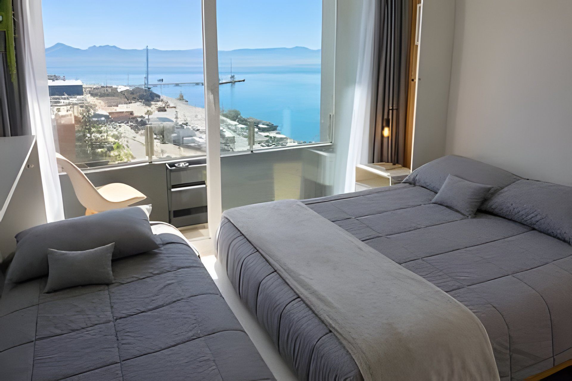 Une chambre d’hôtel avec un grand lit, un lit plus petit et un balcon offrant une vue sur la mer et les montagnes.