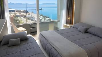 Une chambre d’hôtel avec un grand lit, un lit plus petit et un balcon offrant une vue sur la mer et les montagnes.