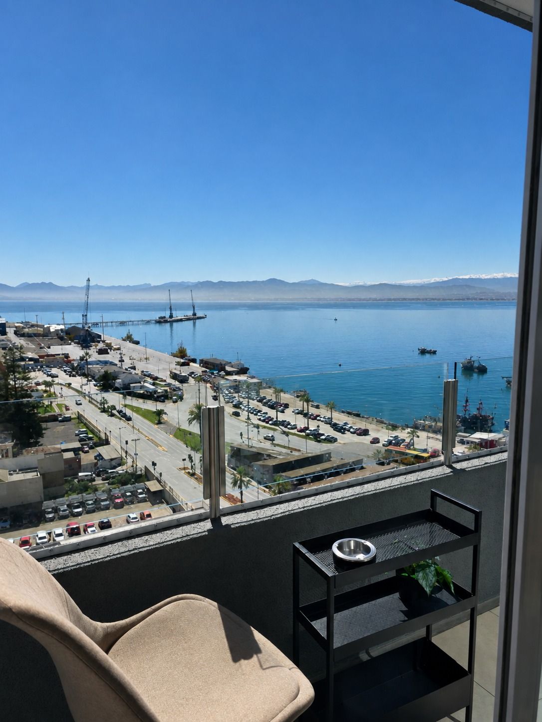 Un balcón con vista a un puerto deportivo, un estacionamiento y montañas a lo lejos.
