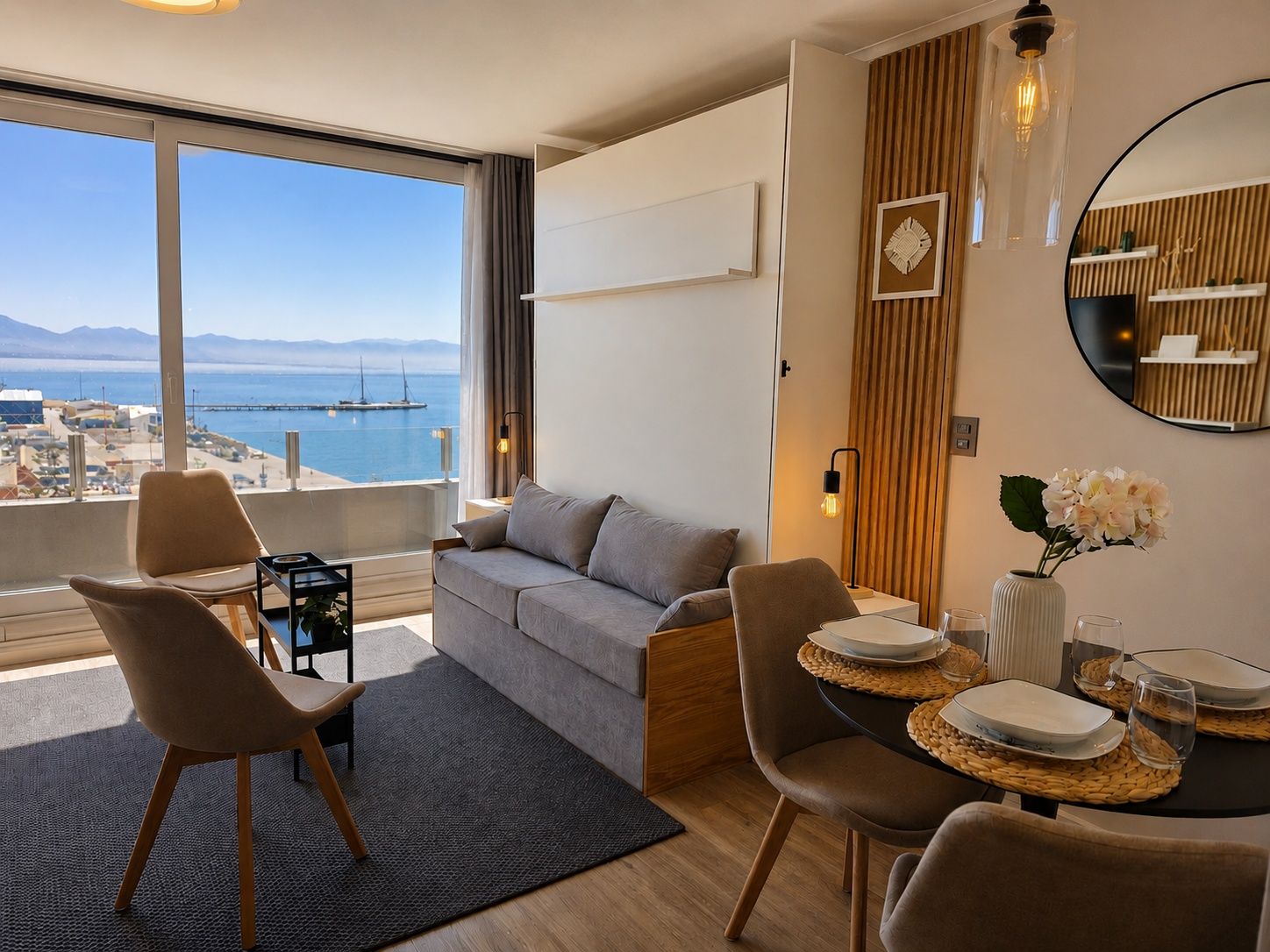 A modern living room with a sofa, chairs, a dining table set, and a view of the sea.