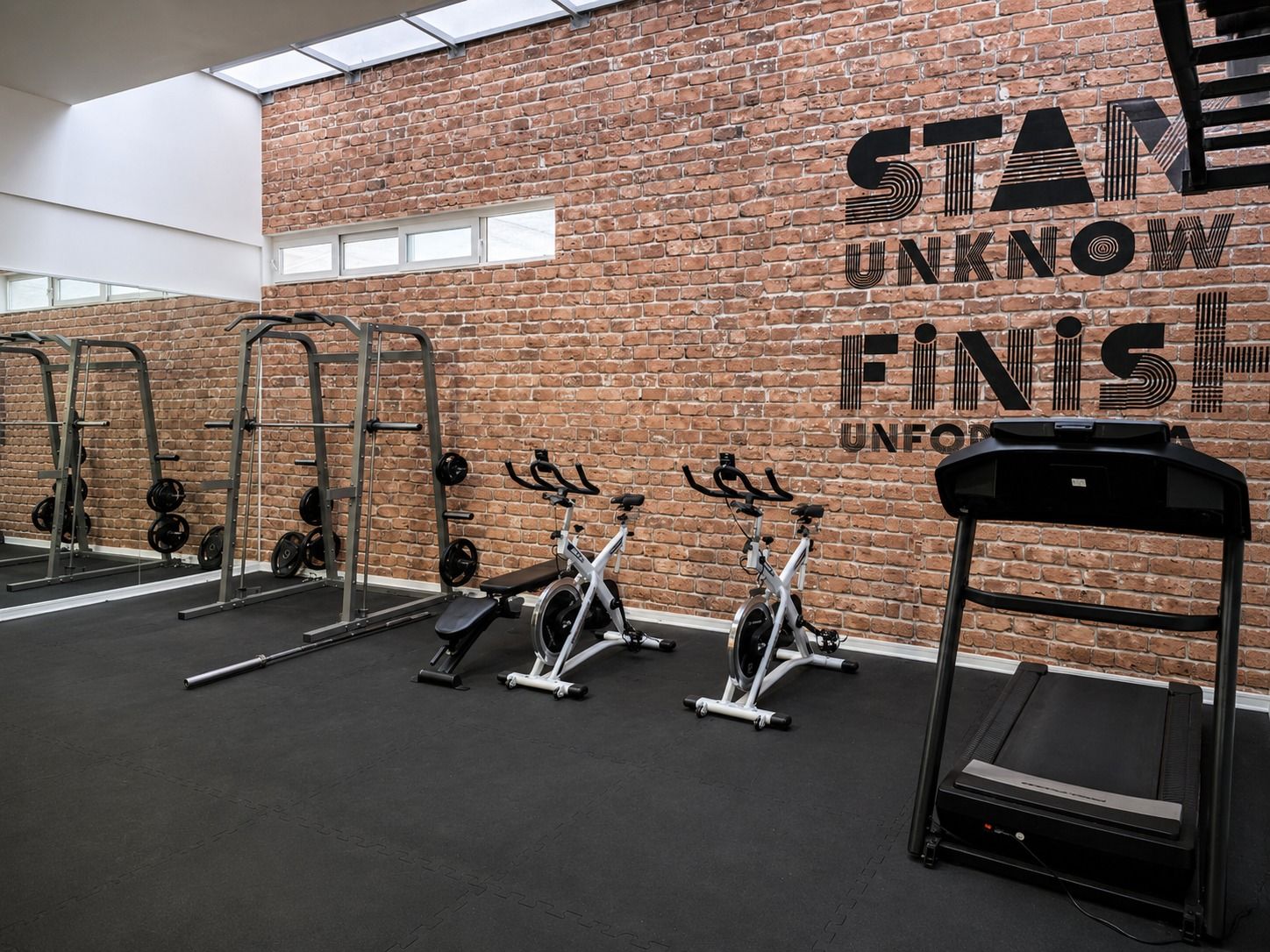 Un gimnasio con paredes de ladrillo, diverso equipo de ejercicio y mensajes motivacionales.