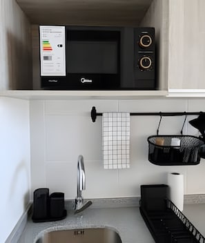 A kitchen with a microwave, a sink, and a hanging rack.