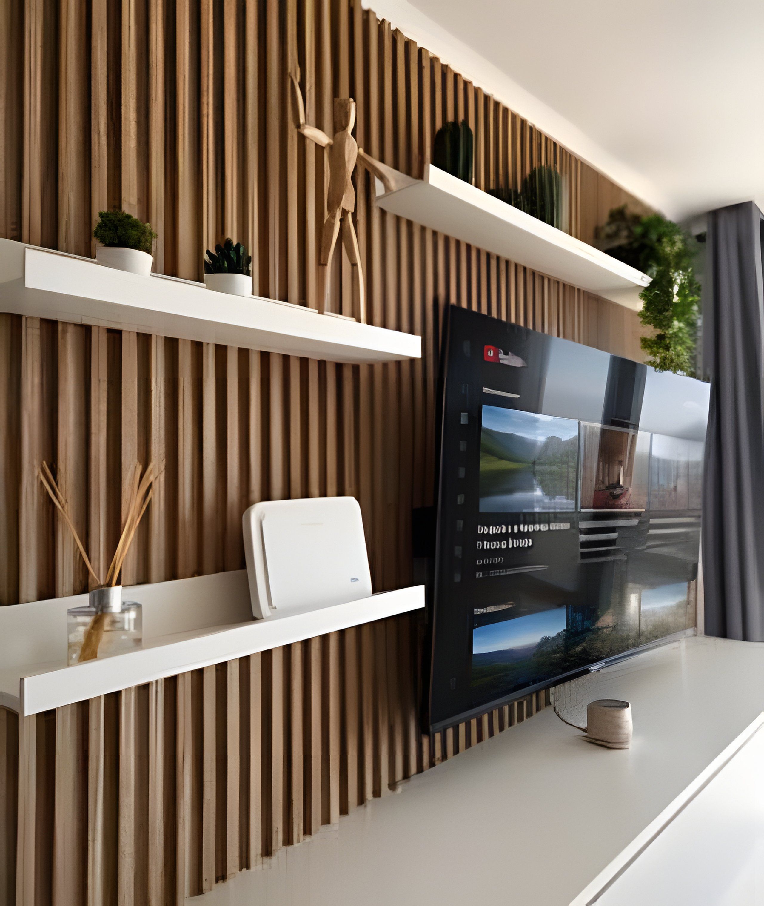 Un salon moderne avec un téléviseur à écran plat fixé au mur, entouré d’étagères blanches où sont disposés des objets décoratifs et des plantes.