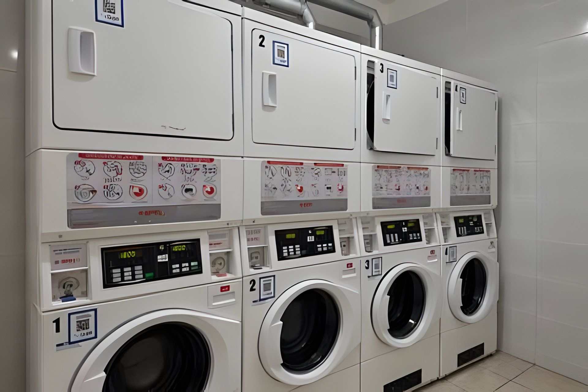 Une rangée de machines à laver blanches, multifonctionnelles, dotées de panneaux de commande et de compartiments numérotés.