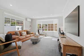 A modern living room with a leather sofa, a round coffee table, and a large flat-screen TV mounted on the wall. - Long Beach Retreat - Stylish 3-bed beach side townhouse! (Sandy Bay)