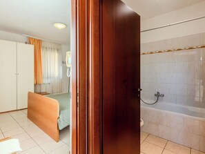 A hotel room with a wooden bed, a bathroom with a bathtub, and a telephone on the wall. - Lovely apartment for 2 people with TV, patio and pets allowed (San Siro)