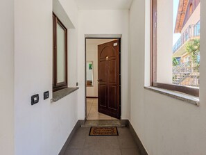 Un pasillo con una puerta de madera, un felpudo y un ventanal con vistas a un edificio.