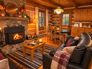 Ein gemütliches Blockhaus-Interieur mit Kamin aus Stein, Ledersofa, Esstisch und Holzeinbauschränken.