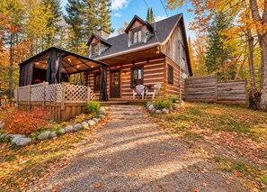 A log cabin with a covered porch, outdoor seating, and a gravel driveway. - Le Shack Shack | Chalet en bois • Spa • Accès au lac (Val-des-Lacs)