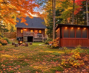 A cabin with a deck and a separate wooden structure, surrounded by autumn foliage. - Le Shack Shack | Chalet en bois • Spa • Accès au lac (Val-des-Lacs)