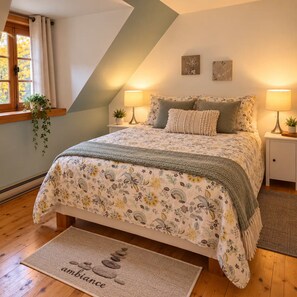 Ein Schlafzimmer mit einem Bett, zwei Nachttischlampen, einem Fenster mit Vorhängen, einer Pflanze und einer Fußmatte mit dem Wort 'ambiance'.