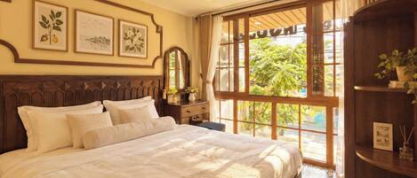 A well-appointed bedroom with a large bed, a dresser, a mirror, and a window with a view of greenery.
