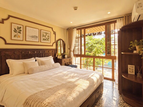 Une chambre bien aménagée, dotée d’un grand lit, d’une commode, d’un miroir et d’une fenêtre donnant sur un paysage verdoyant.