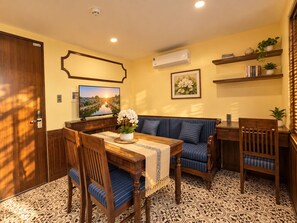 A room with a wooden dining table, blue-striped sofa, and a television displaying a scenic view. - Lunaria Indochine Apartments (An Hai)